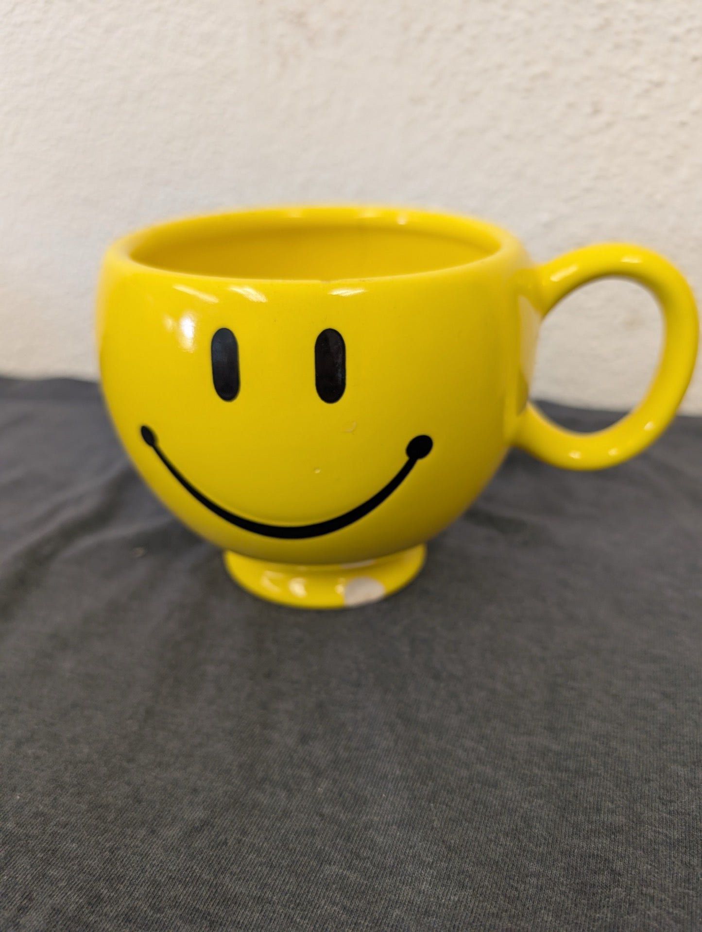 Bright yellow ceramic coffee mug with a black classic smiley face printed on it.