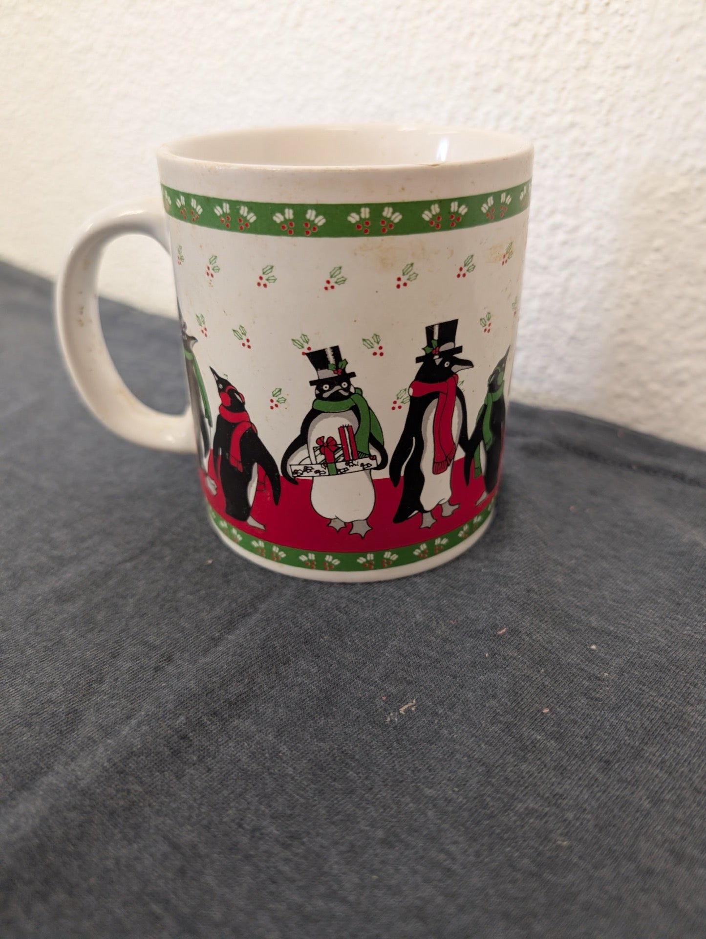 White ceramic mug decorated with a red border and cute penguins wearing winter clothes.