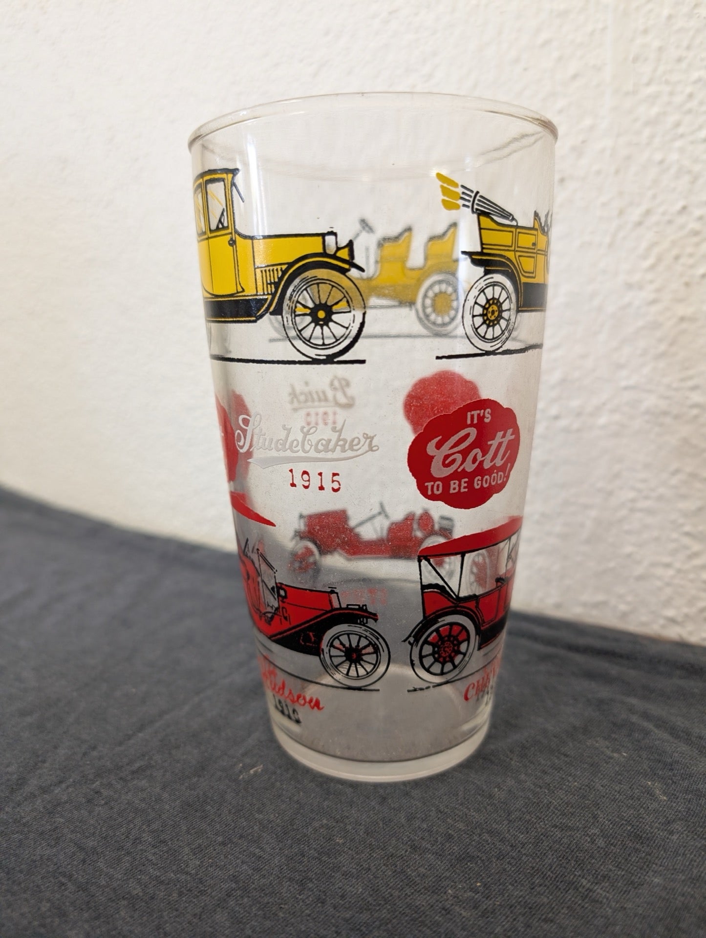 Clear glass tumbler printed with yellow and red antique cars and a Cott Beverages logo.
