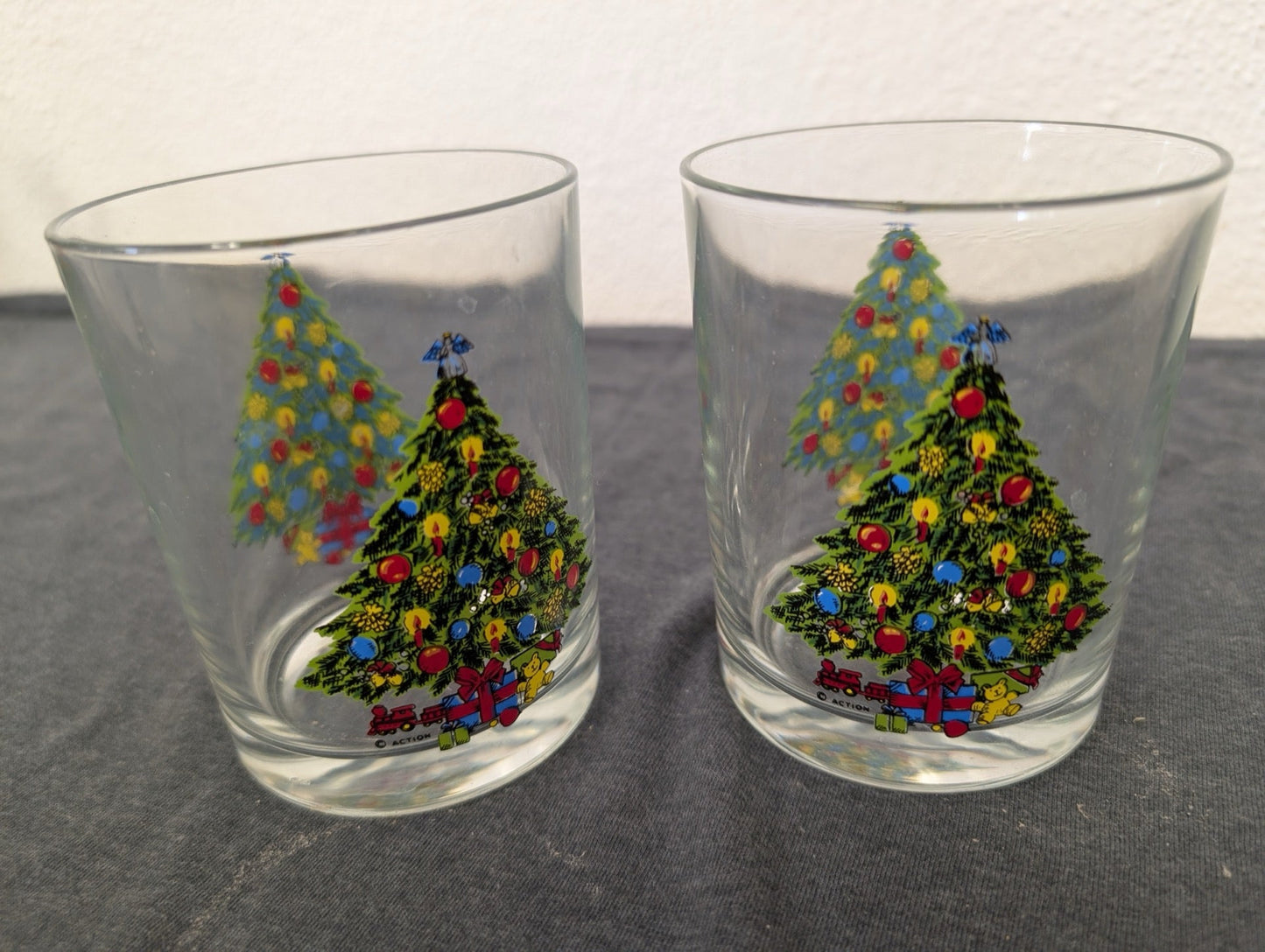 Two clear lowball glasses featuring a decorated Christmas tree and toy train graphic.