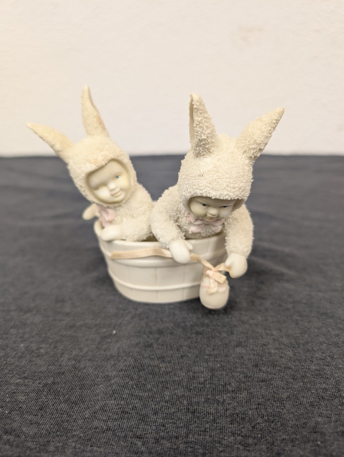 Two textured ceramic snowbabies wearing hoods sitting in a white basket.