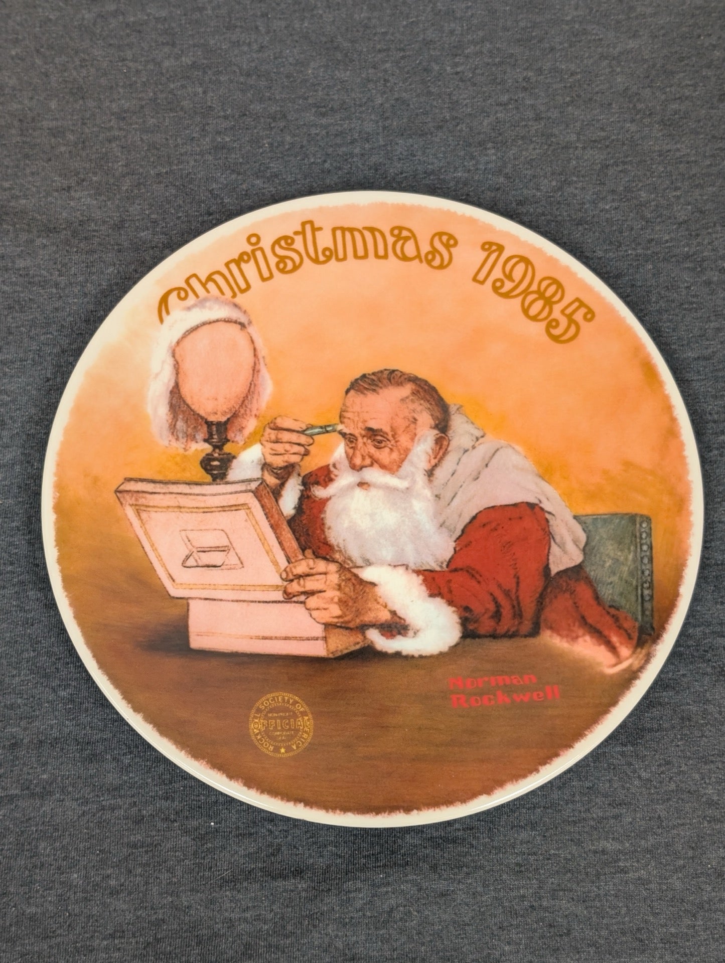 Round collector plate depicting Santa Claus looking at a globe by Norman Rockwell, labeled Christmas 1985.