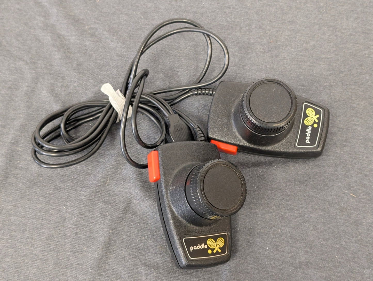 Pair of black vintage Atari 2600 paddle controllers with wires.