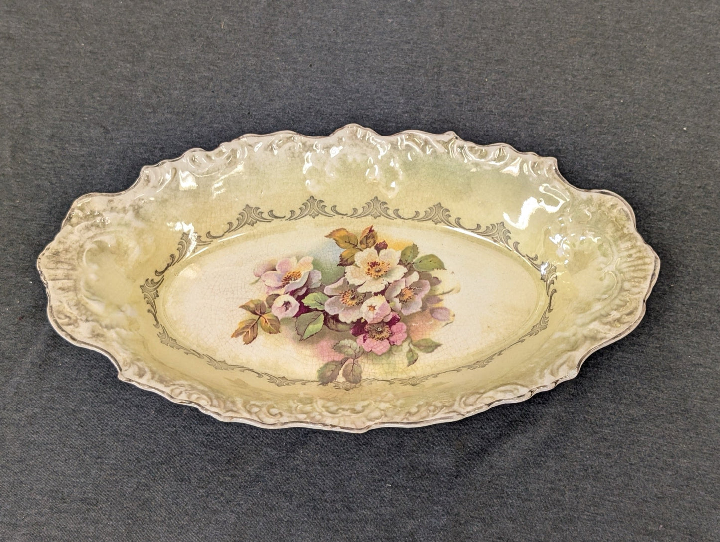 Oval ceramic serving platter with a scalloped edge, a central floral bouquet design, gray borders, and noticeable surface crazing.