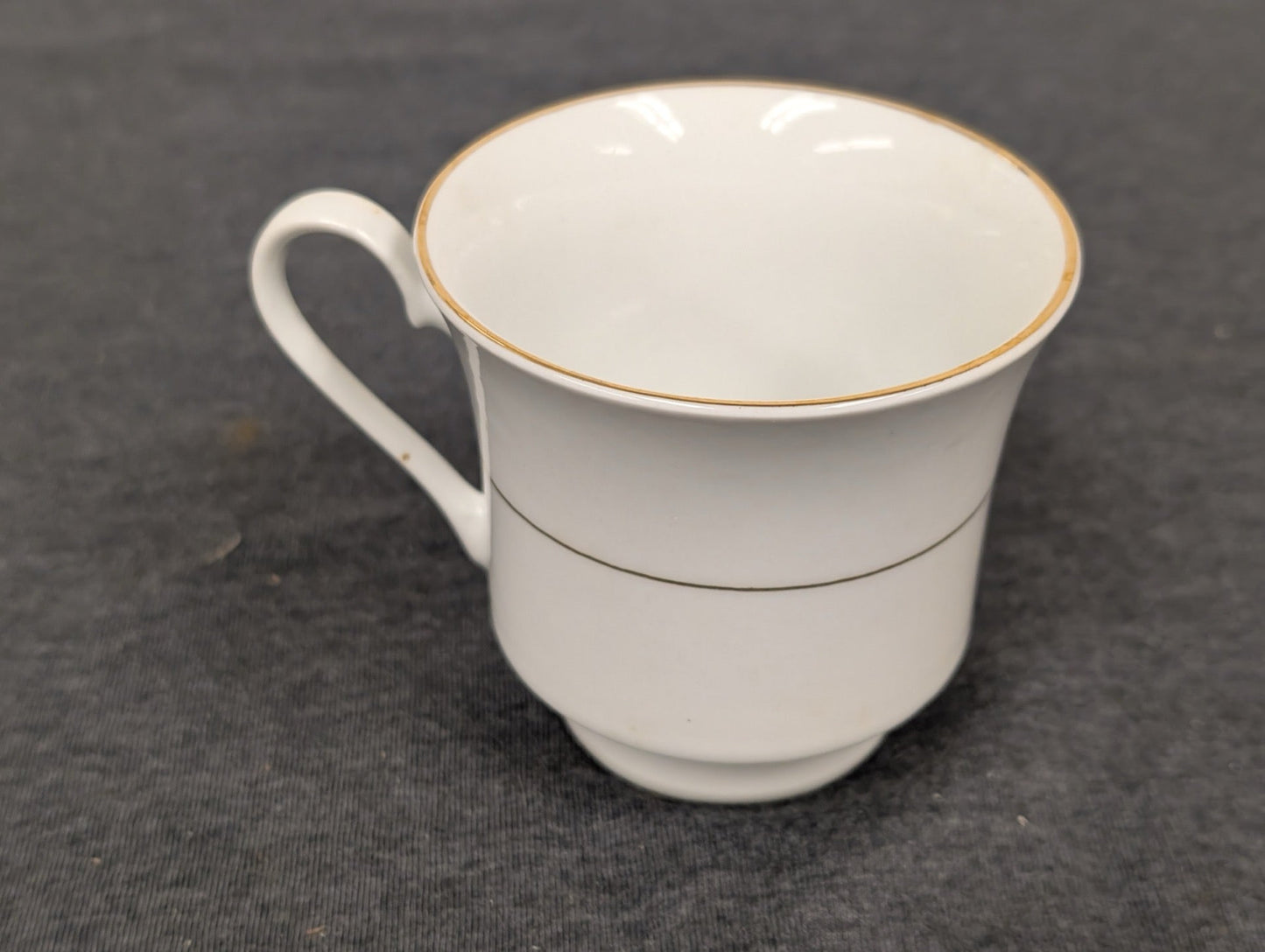 Angled view of a white teacup with gold rim and center stripe