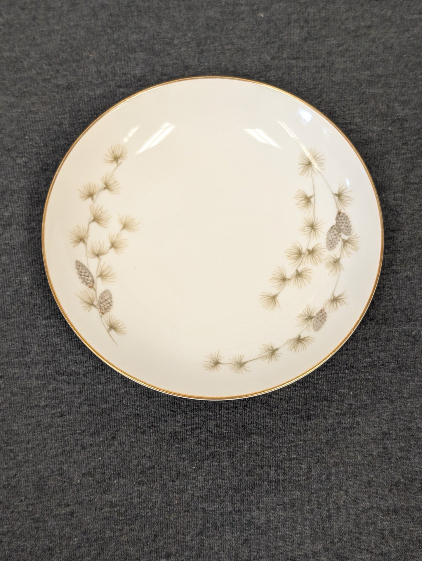 Full front view of the white plate with pinecone and pine needle motif.