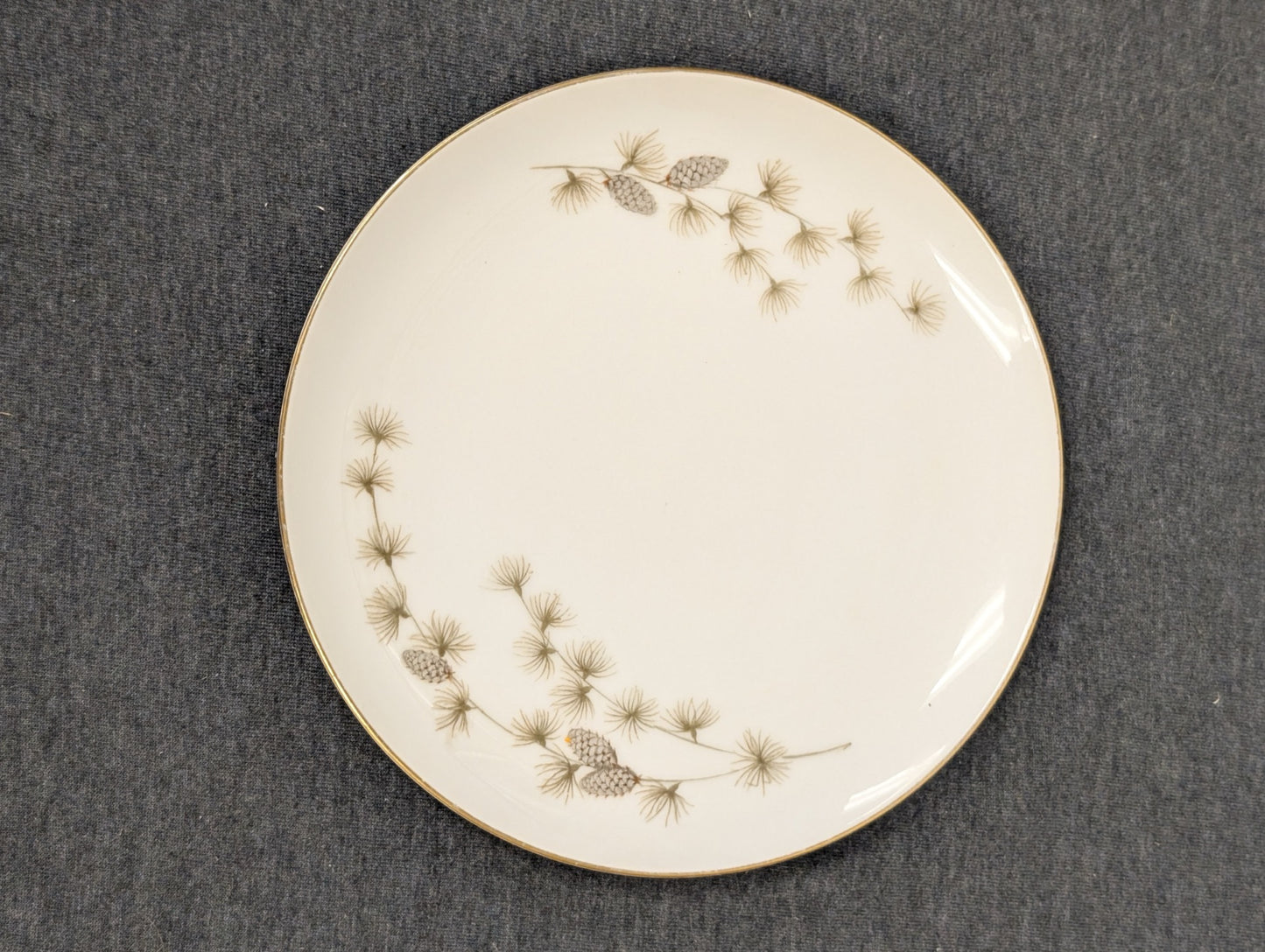 White vintage dinner plate featuring a pinecone and pine needle border design.