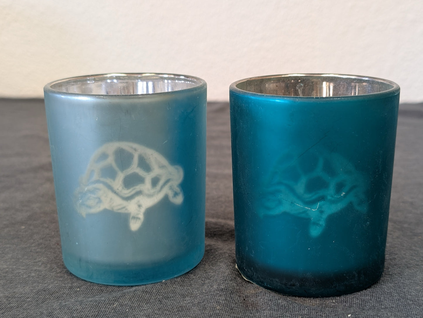 Two frosted glass votive candle holders with sea turtle design in dark and light blue
