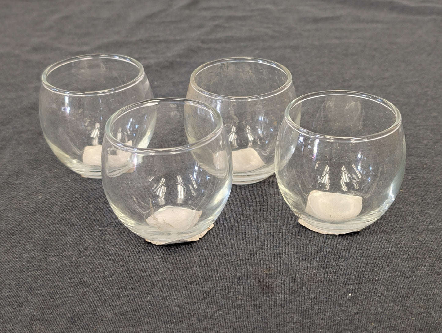 Set of four small round clear glass votive holders on a grey background