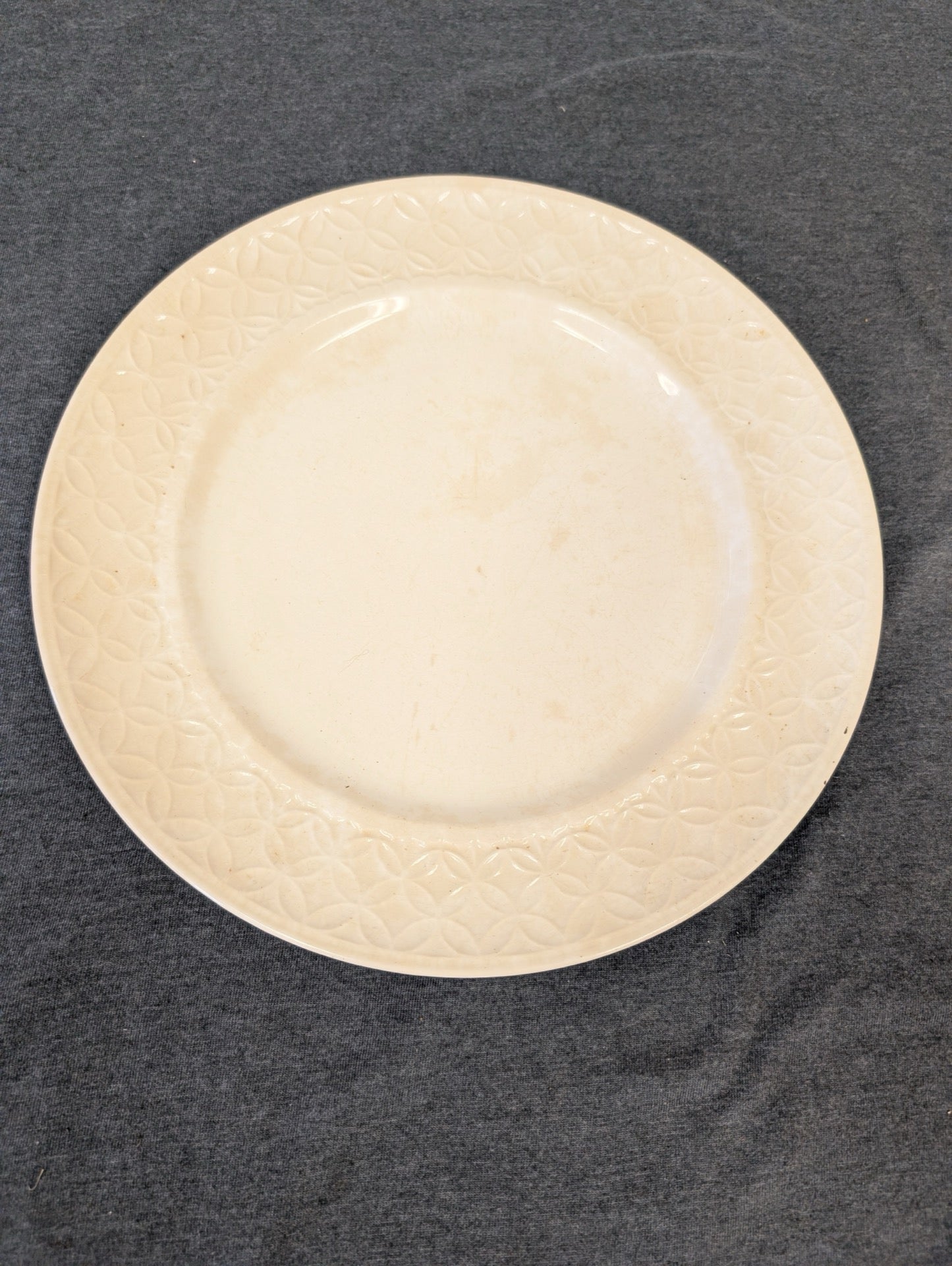 Cream colored vintage plate with an embossed geometric border in good condition.