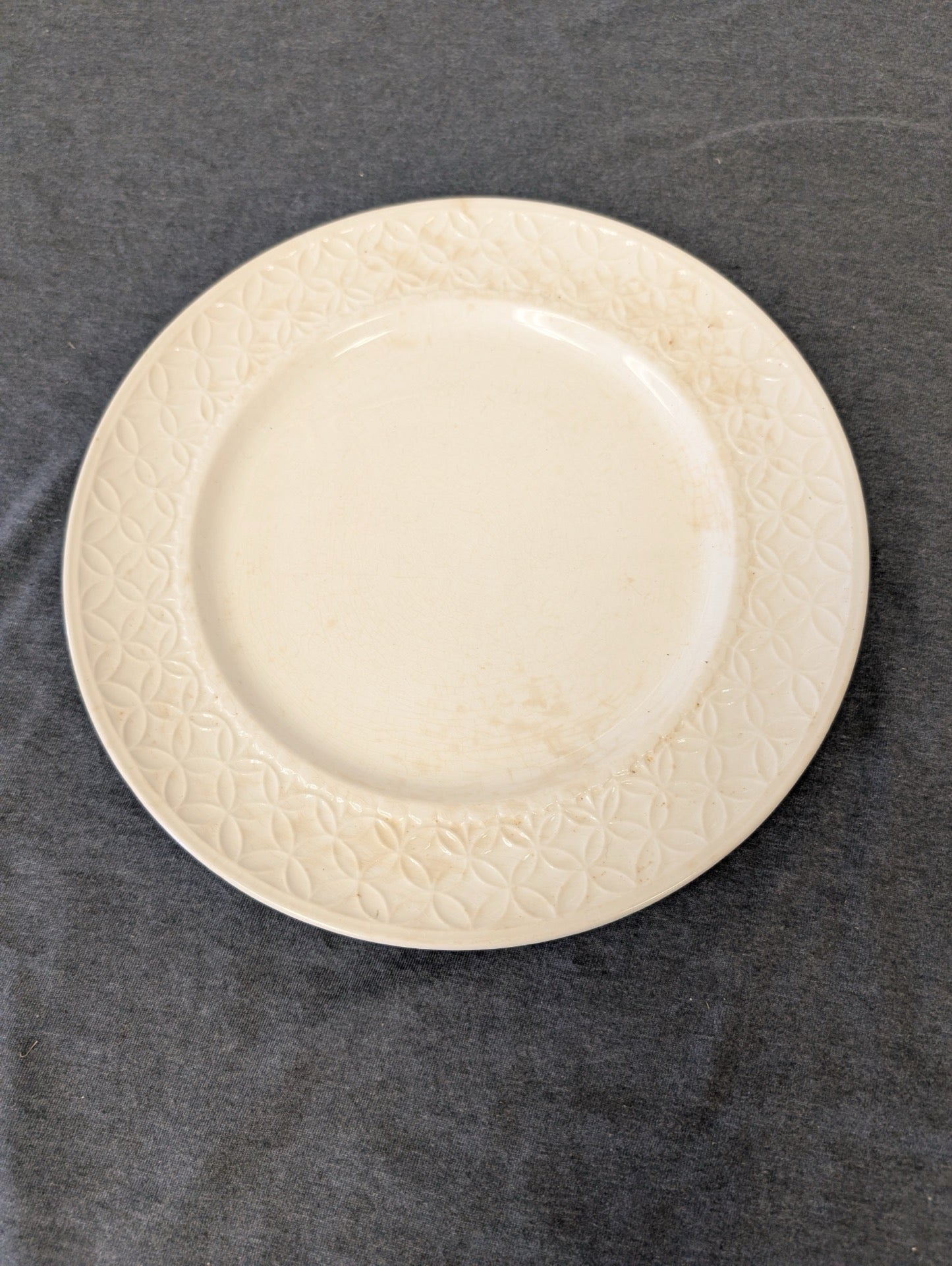 Vintage cream plate with a geometric embossed rim showing slight wear marks.
