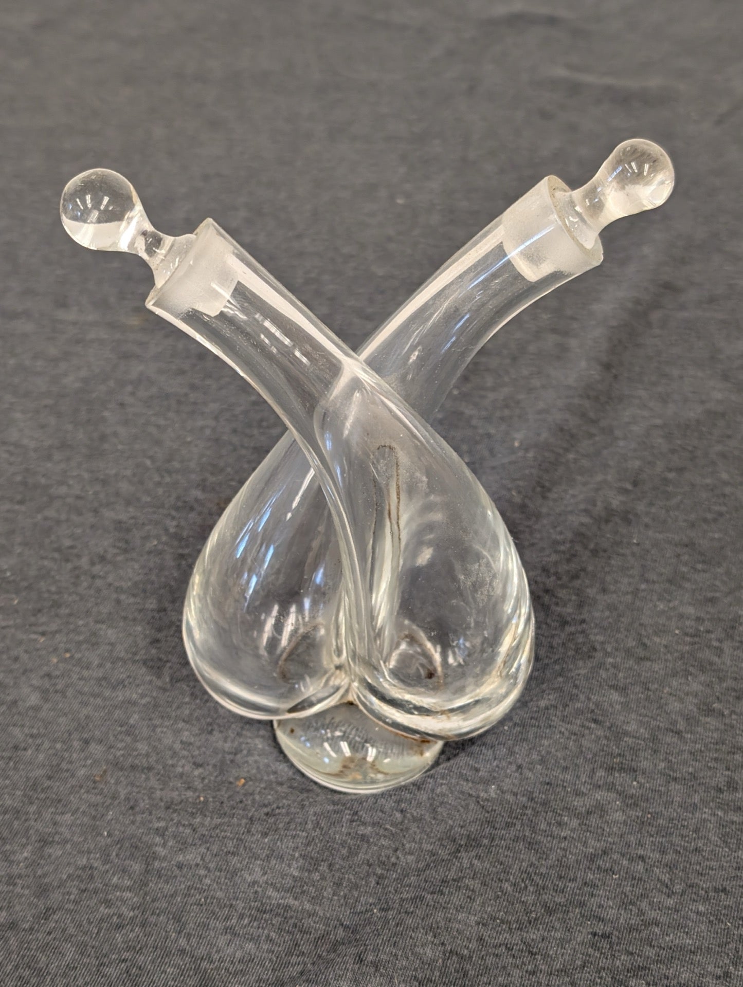 Clear glass double cruet with criss-crossing necks and two glass stoppers.