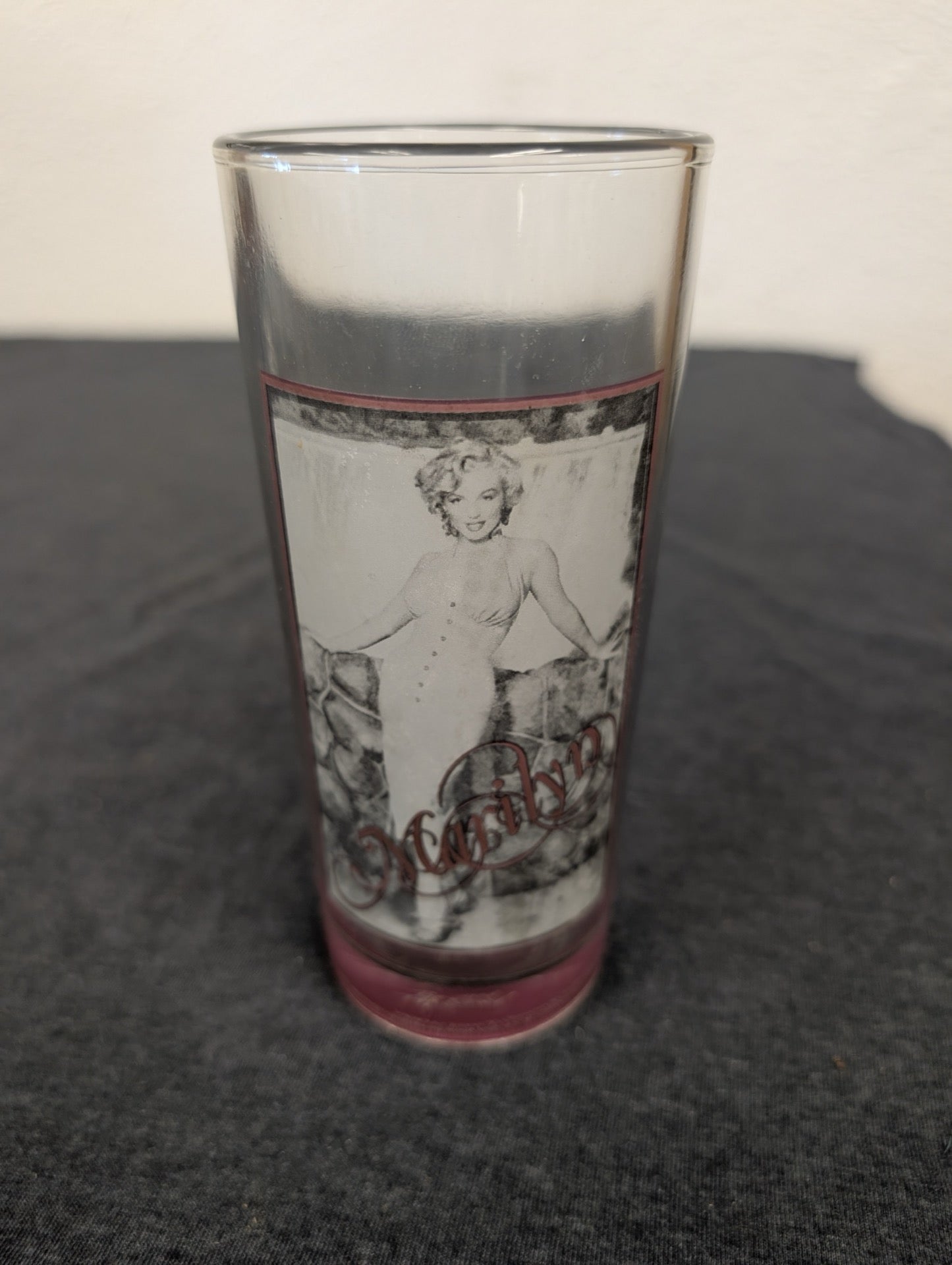 Clear glass showing Marilyn Monroe in a white dress against a stone wall background