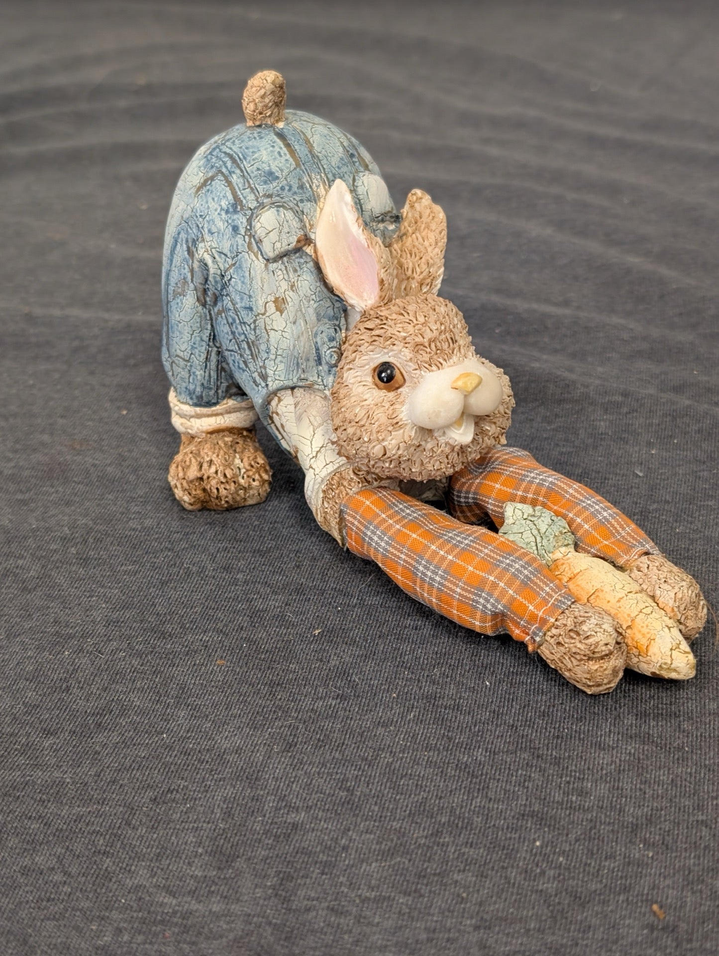 Resin rabbit wearing blue overalls stretching out holding a carrot