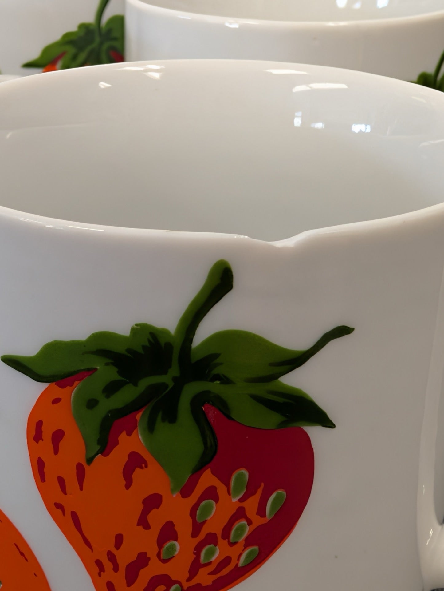 Close-up of a white mug with a strawberry pattern showing a small chip on the rim.
