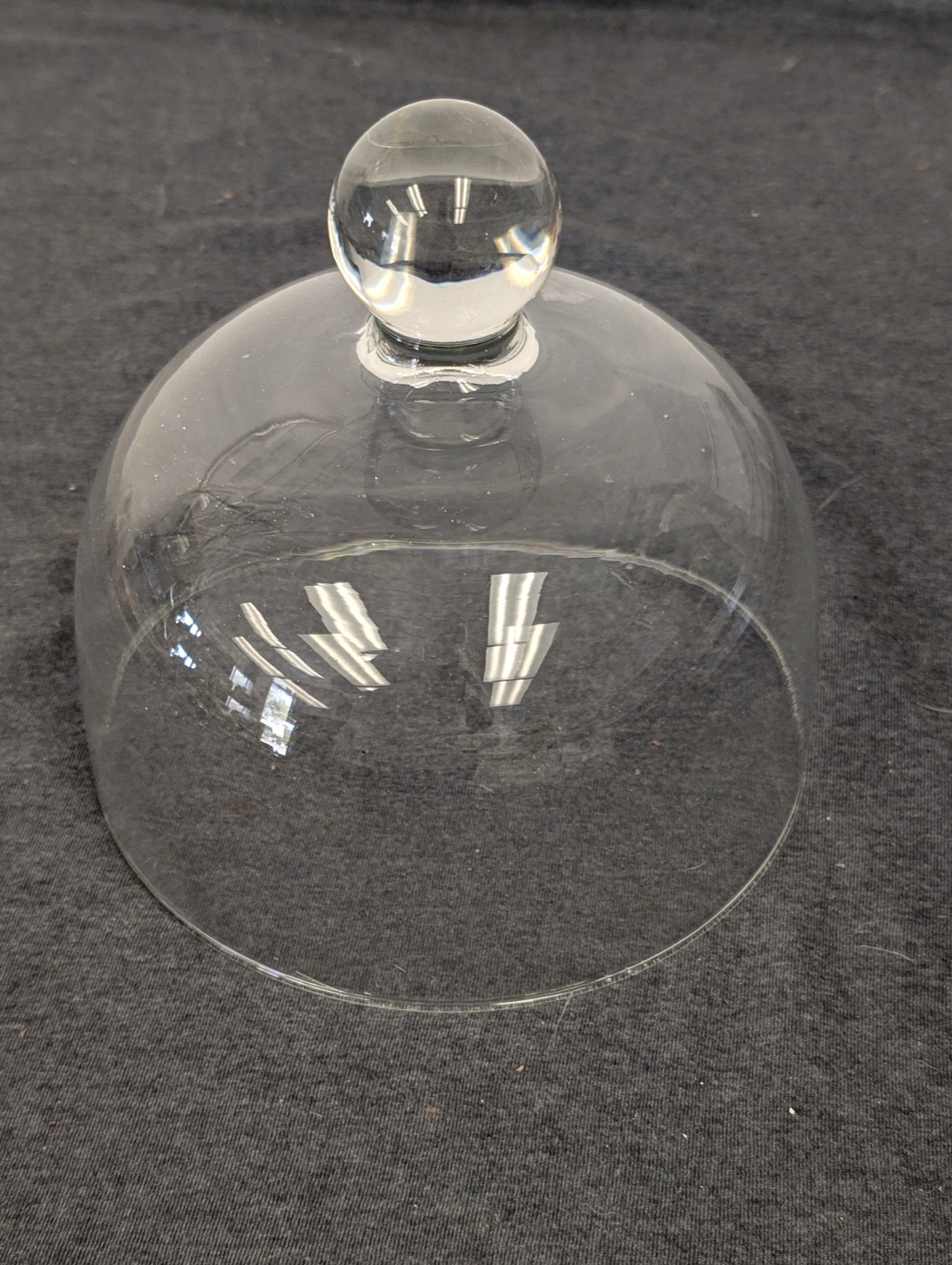 Clear glass cloche dome with a round ball knob on top resting on a gray surface.
