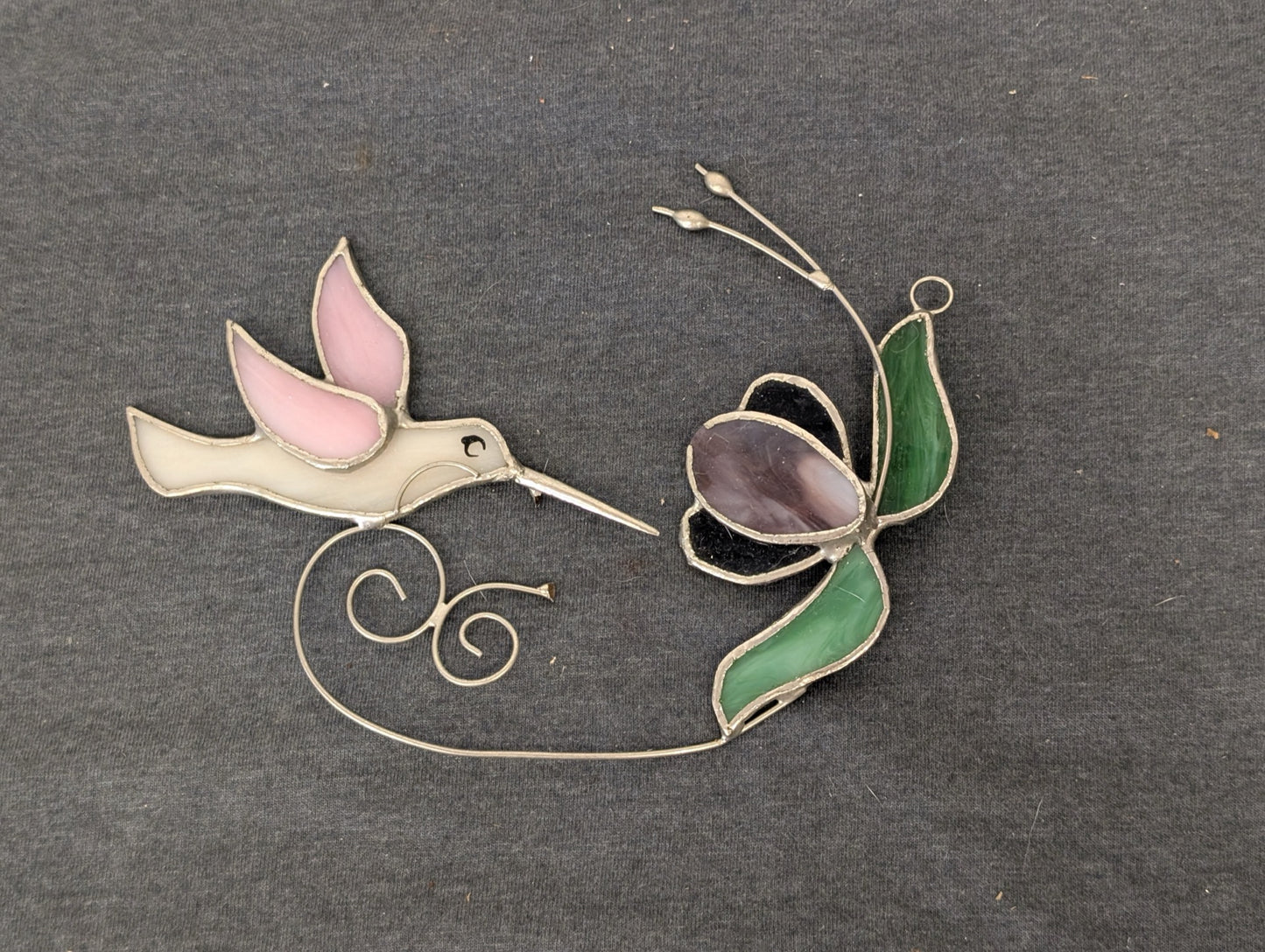 Stained glass art piece depicting a pink and white hummingbird and a purple flower connected by wire.