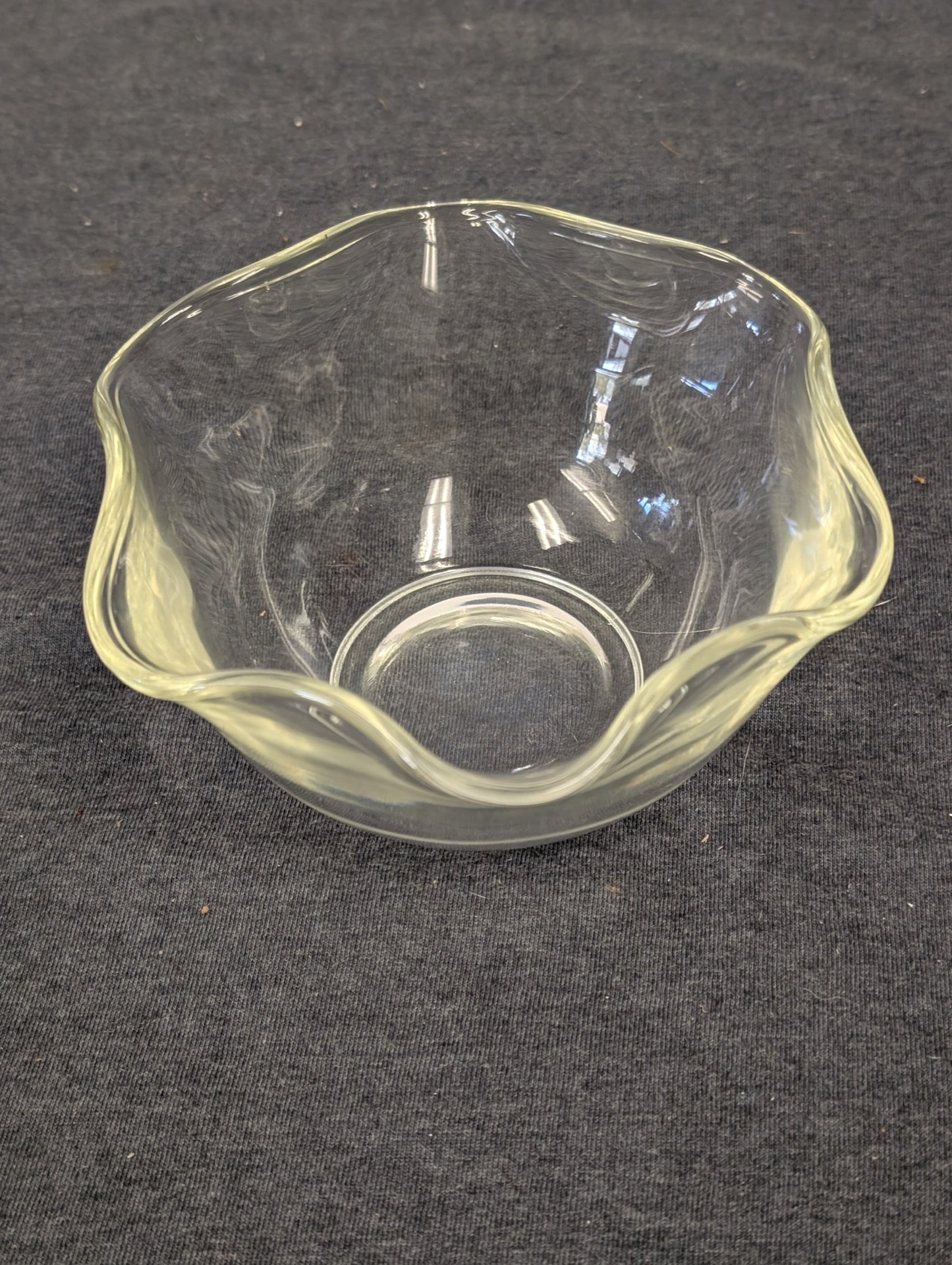 Small clear glass bowl with a scalloped, wavy edge sitting on a dark surface.