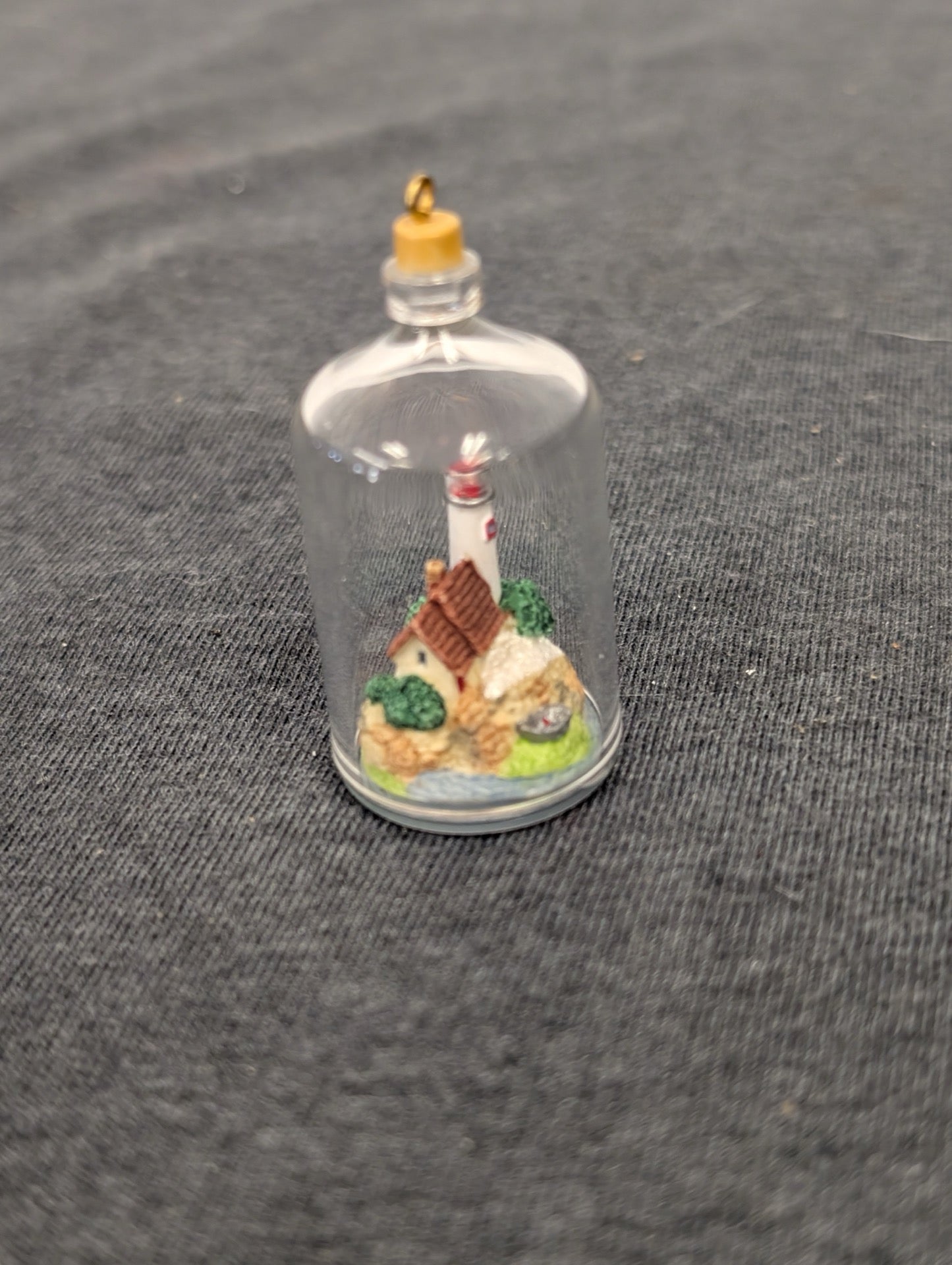 A tiny lighthouse and small house built on a rock structure inside a clear glass bottle.