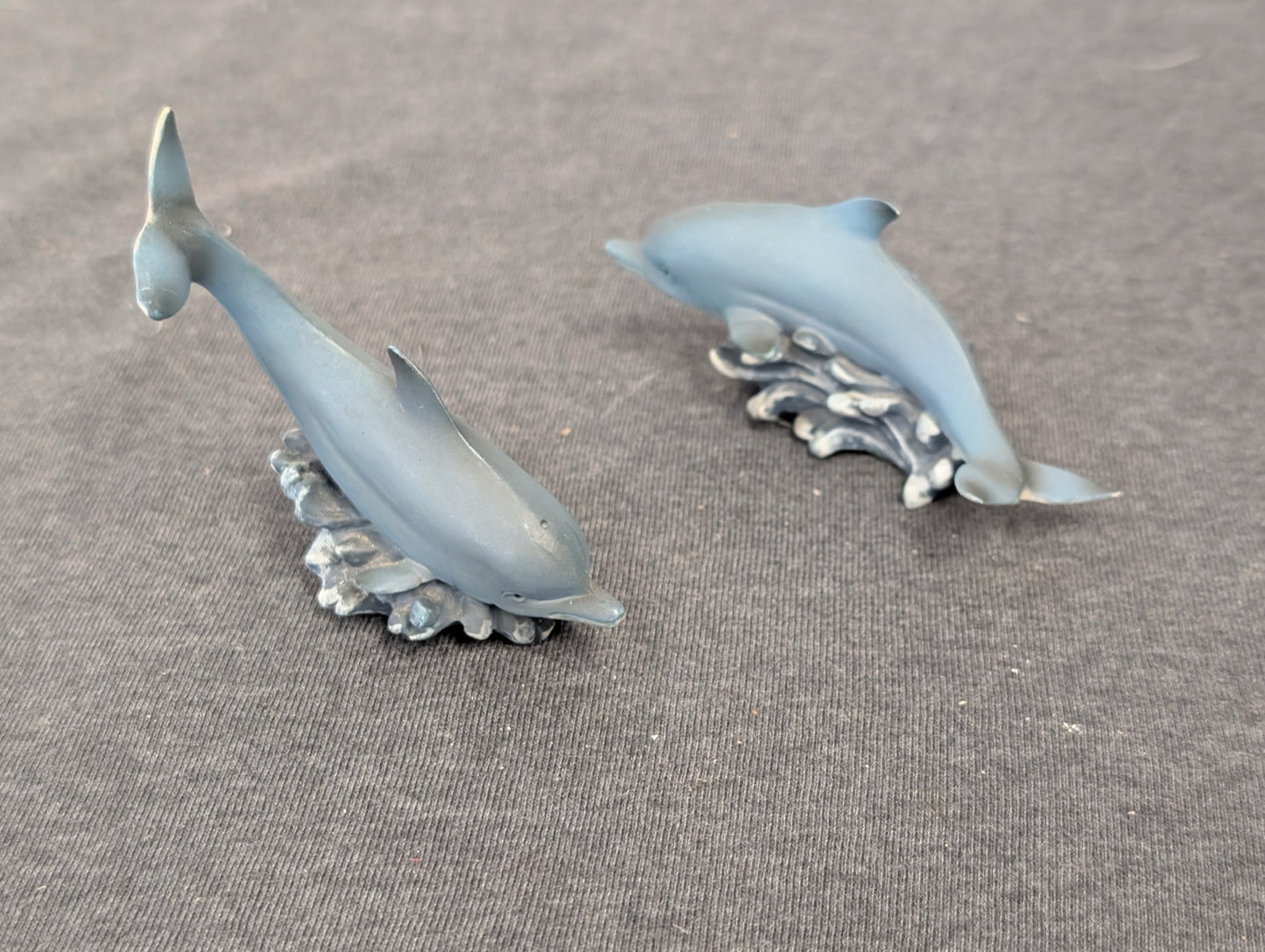 Two small grey dolphin figurines, one diving and one swimming, over small wave bases.