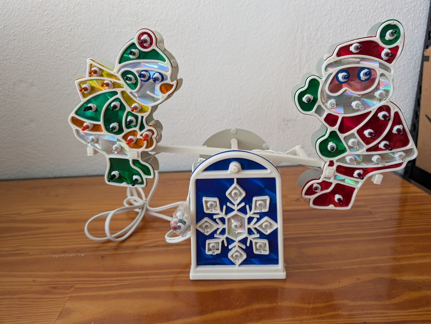 Santa & Angel Seesaw Light from Unknown (Possibly H.C. Company or a similar brand) - 1980s-1990s Holiday Decor (Plastic, Holographic Foil, Wiring Christmas Light Decoration, Christmas, Holiday, Retro, Kitsch, White, Red, Green, Blue, Yellow)
