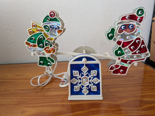 Santa & Angel Seesaw Light from Unknown (Possibly H.C. Company or a similar brand) - 1980s-1990s Holiday Decor (Plastic, Holographic Foil, Wiring Christmas Light Decoration, Christmas, Holiday, Retro, Kitsch, White, Red, Green, Blue, Yellow)