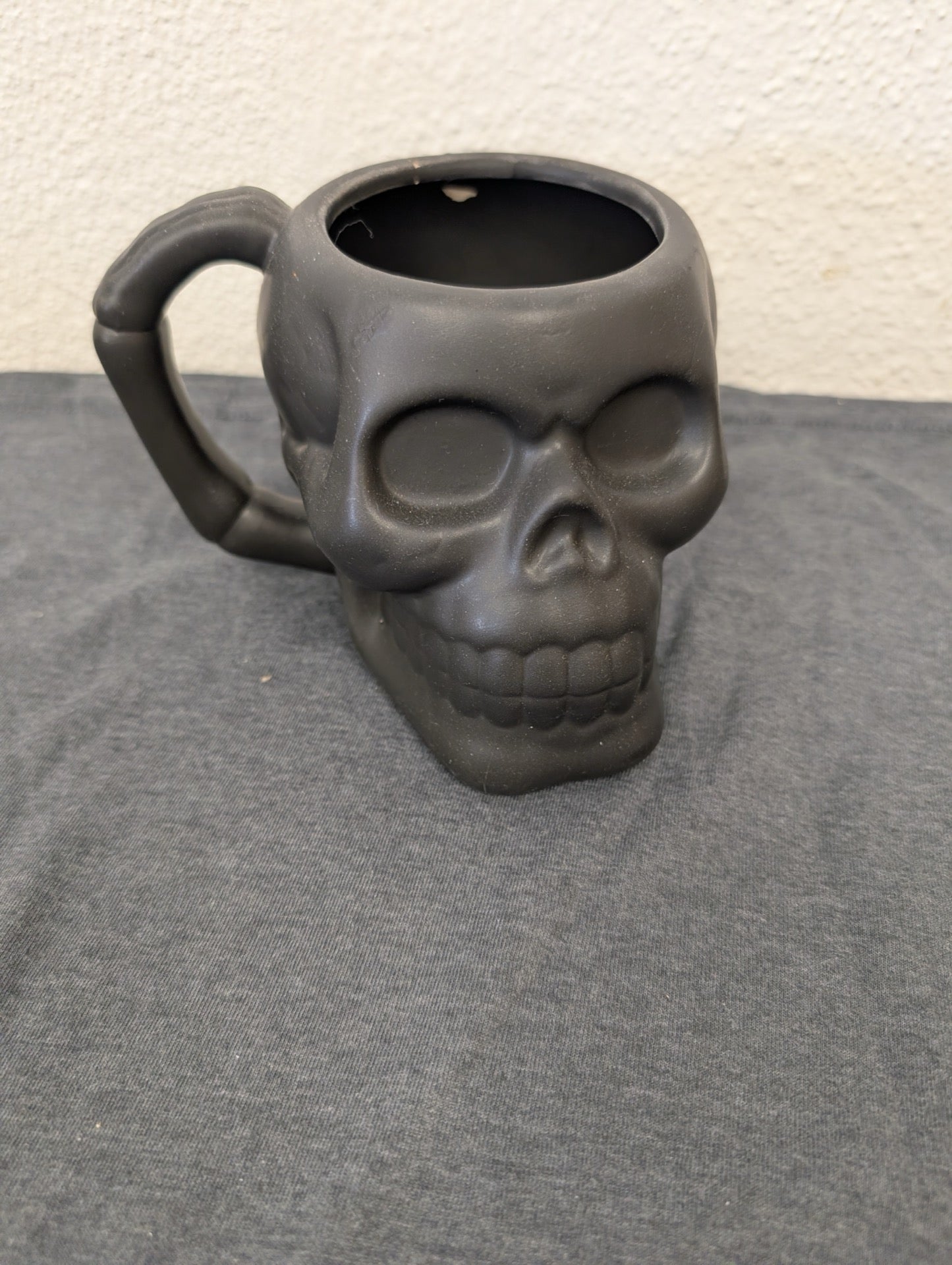Matte black ceramic coffee mug shaped like a human skull with a bone handle.