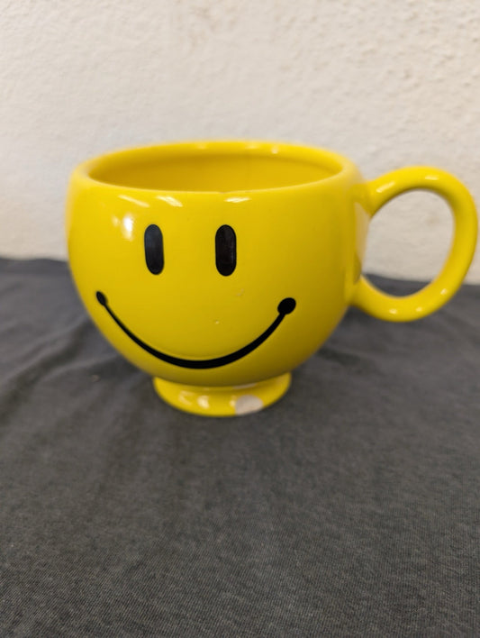 Bright yellow ceramic coffee mug with a black classic smiley face printed on it.