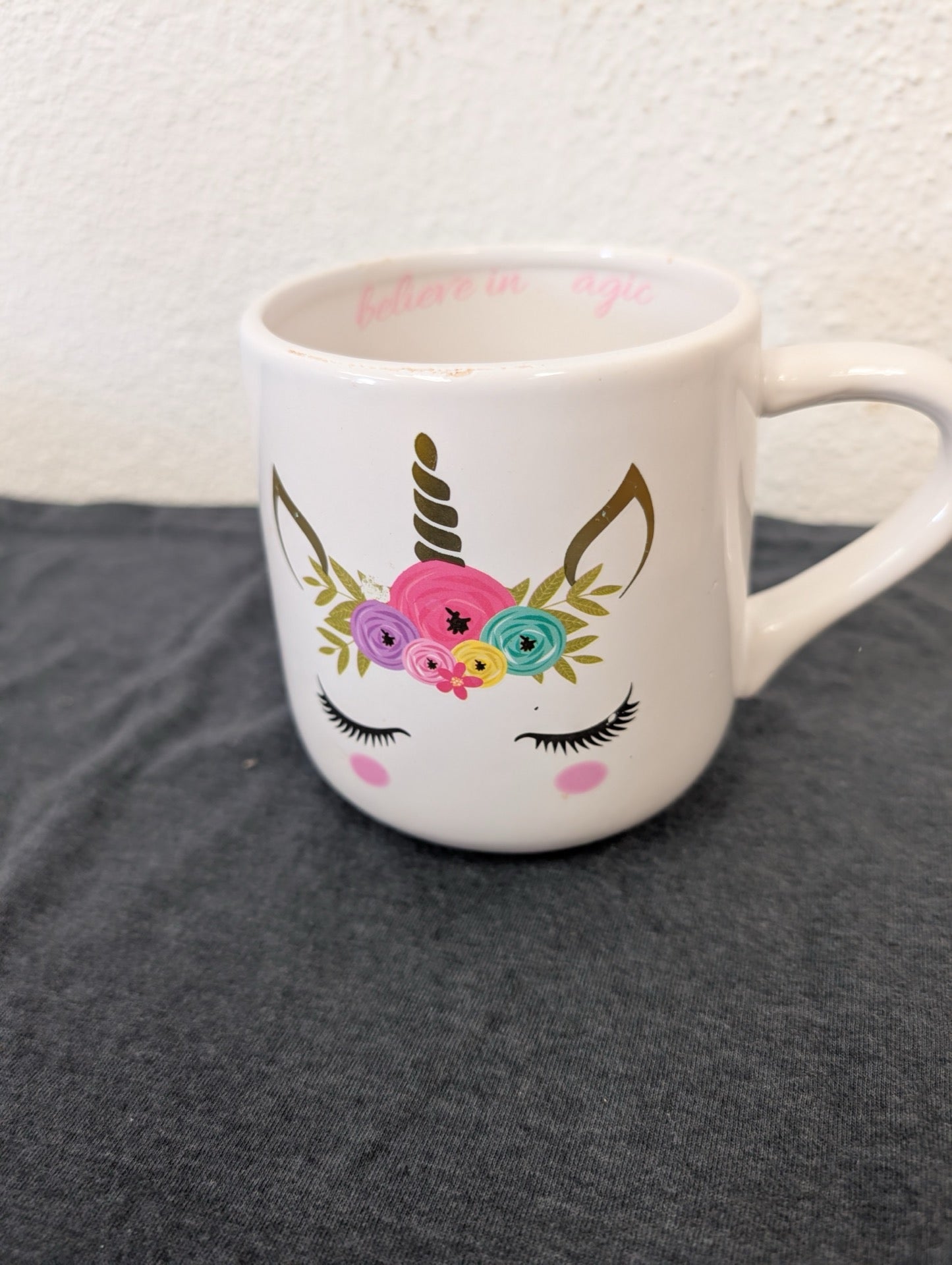 White ceramic mug featuring a unicorn face with eyelashes, a gold horn, and a flower crown.