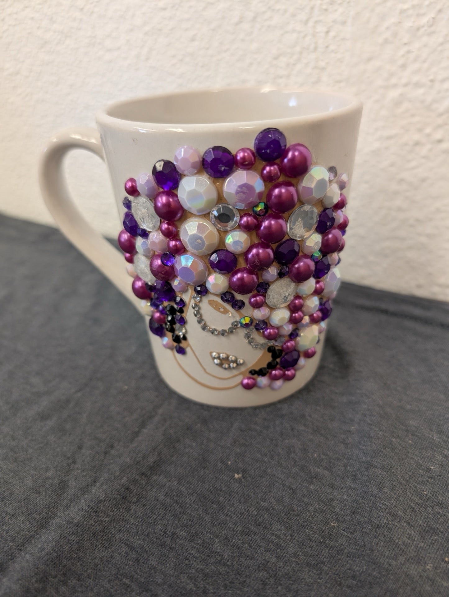 White coffee mug decorated with purple and clear rhinestones forming a woman's hair.