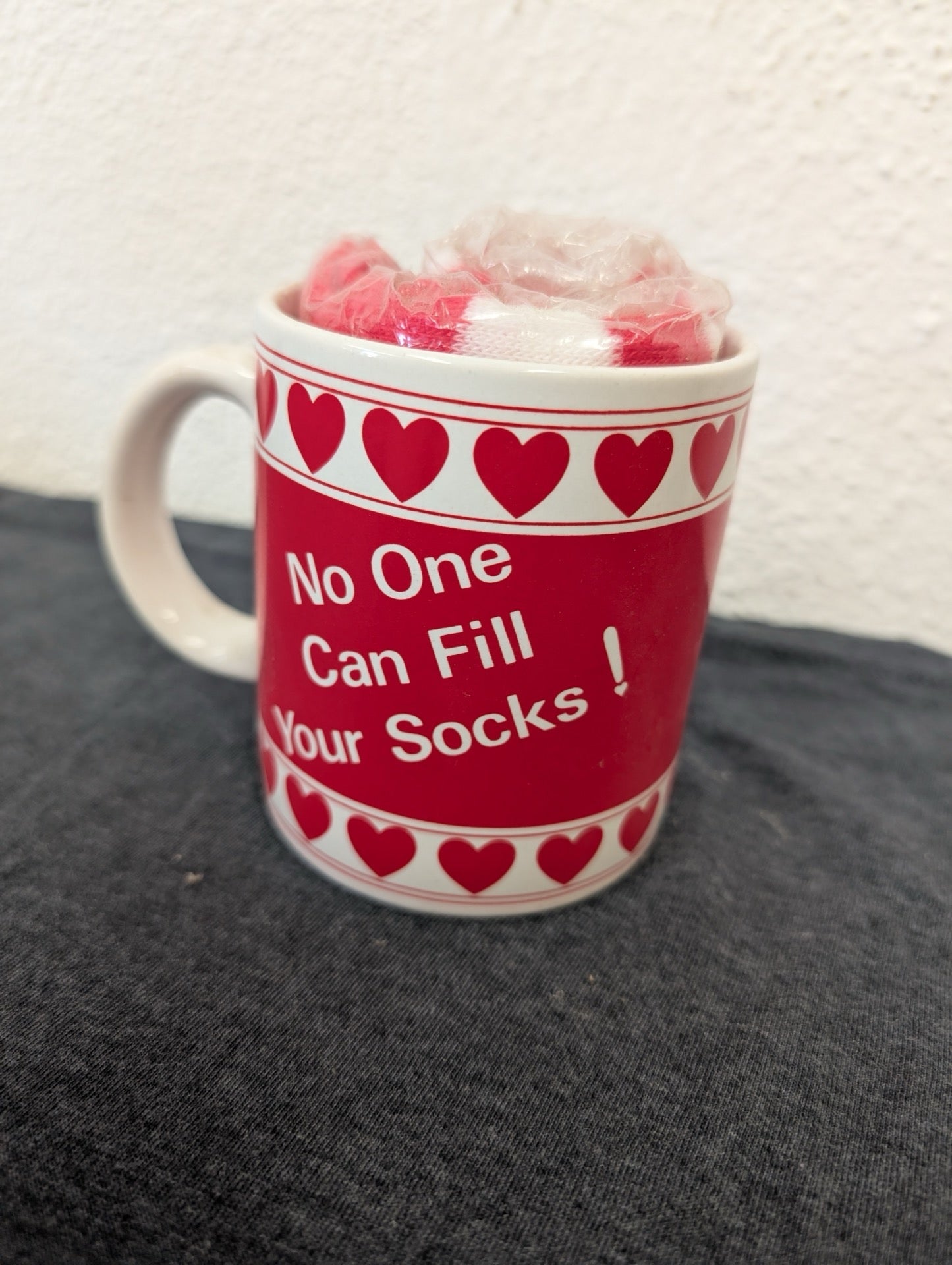 Red ceramic mug with white text saying No One Can Fill Your Socks and rolled socks inside.