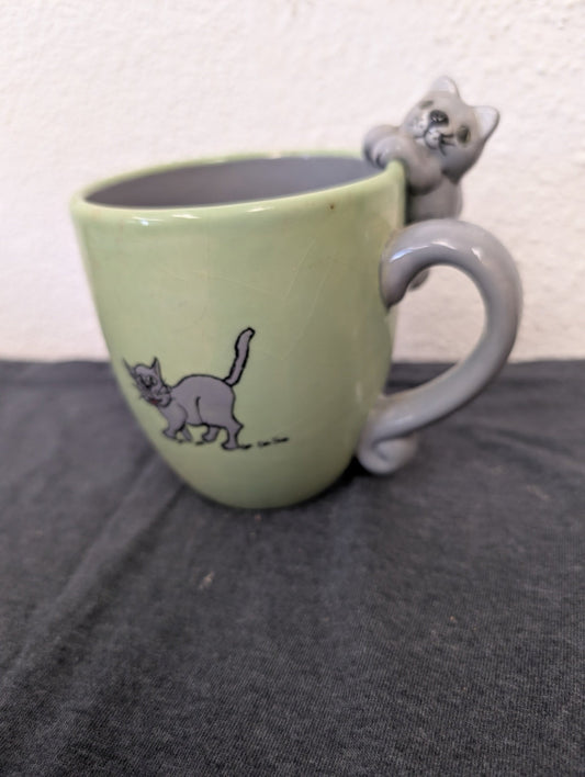 Light green ceramic mug featuring a drawing of a cat and a 3D cat figure forming the handle.
