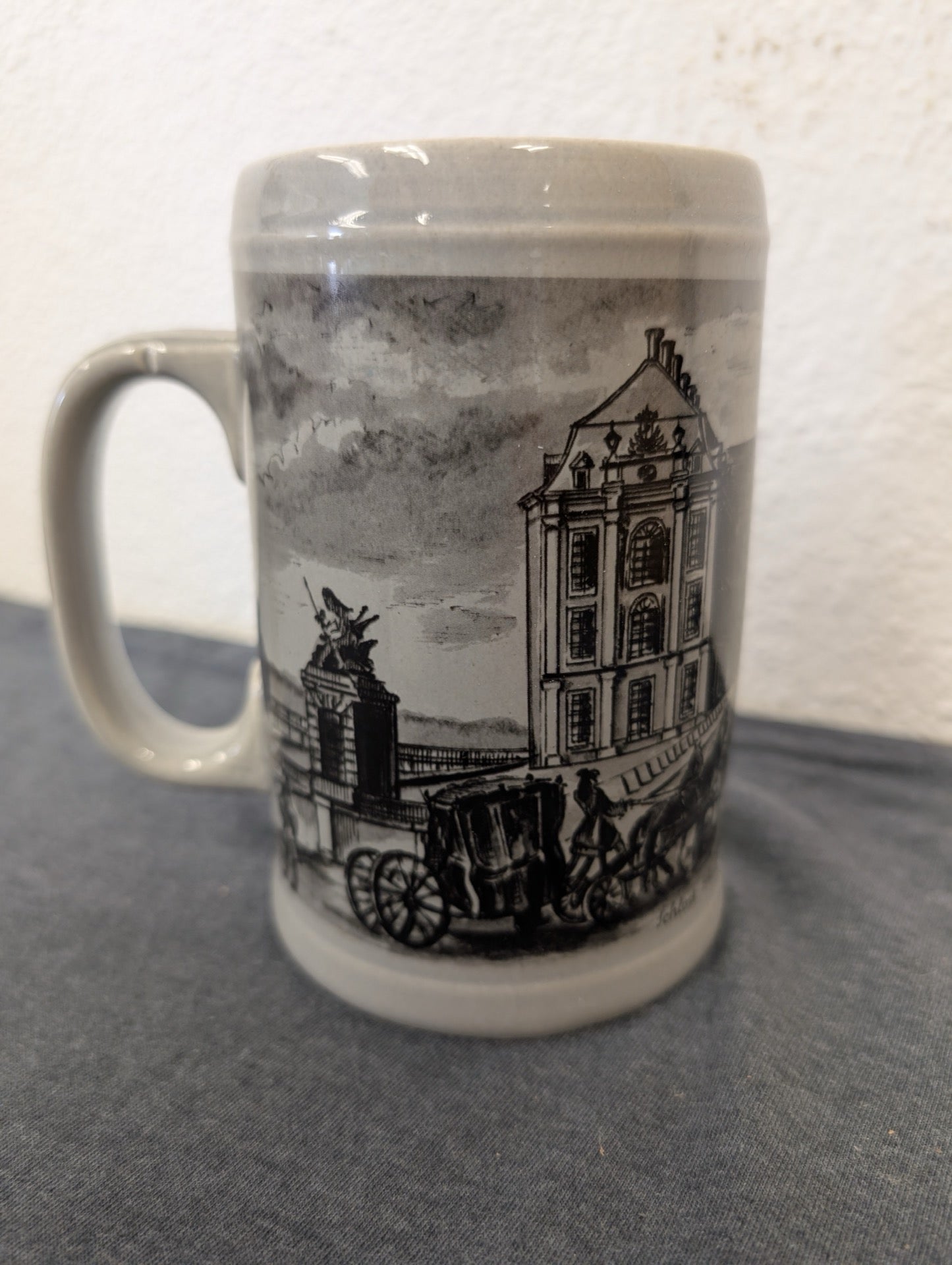 Greyish ceramic stein with a detailed black ink style drawing of a historical palace and carriage.