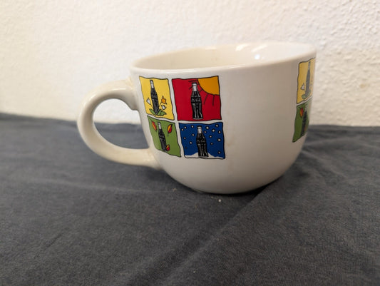 Wide white mug with four colorful squares showing a Coca-Cola bottle in different seasons.