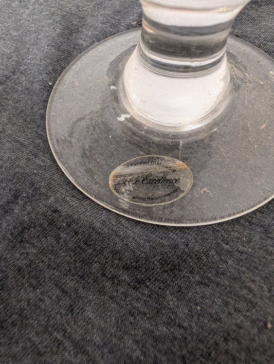 Close-up of a clear glass stemware base with a Table Excellence Hand Painted Glassware sticker.