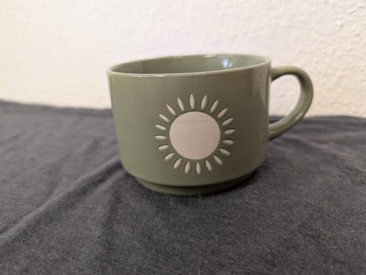 Light olive green ceramic coffee mug with a white circular sunburst design.