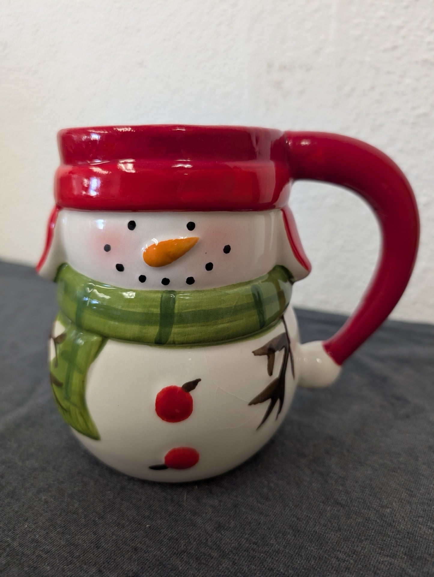 Ceramic 3D mug shaped like a snowman face with a red winter hat rim and a green scarf.