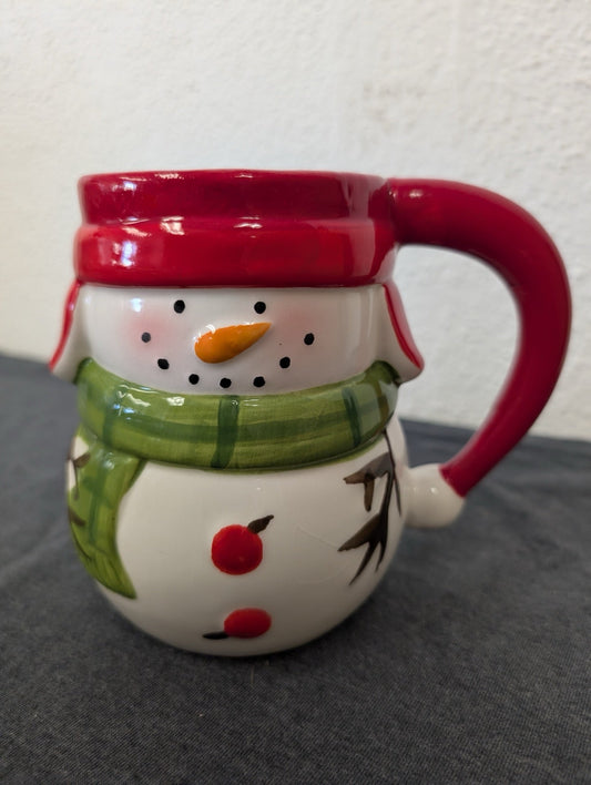 Ceramic 3D mug shaped like a snowman face with a red winter hat rim and a green scarf.