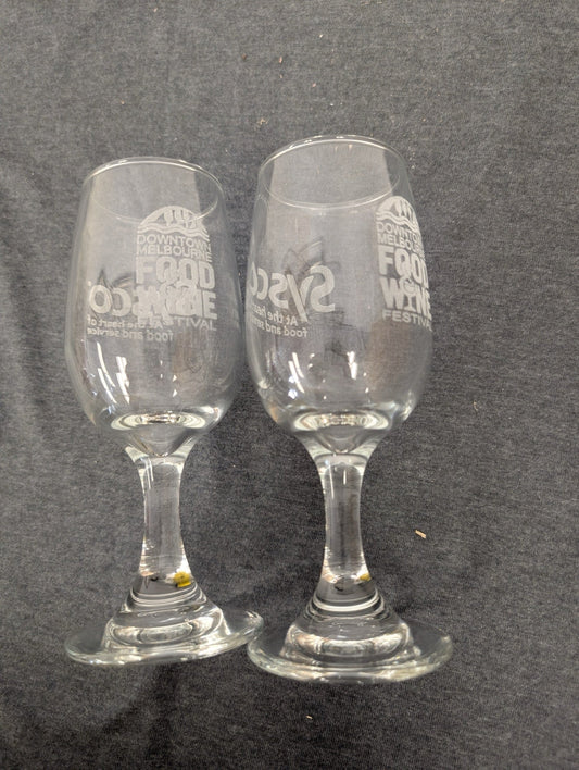 Two clear stemmed wine tasting glasses etched with the Downtown Melbourne Food and Wine Festival logo.