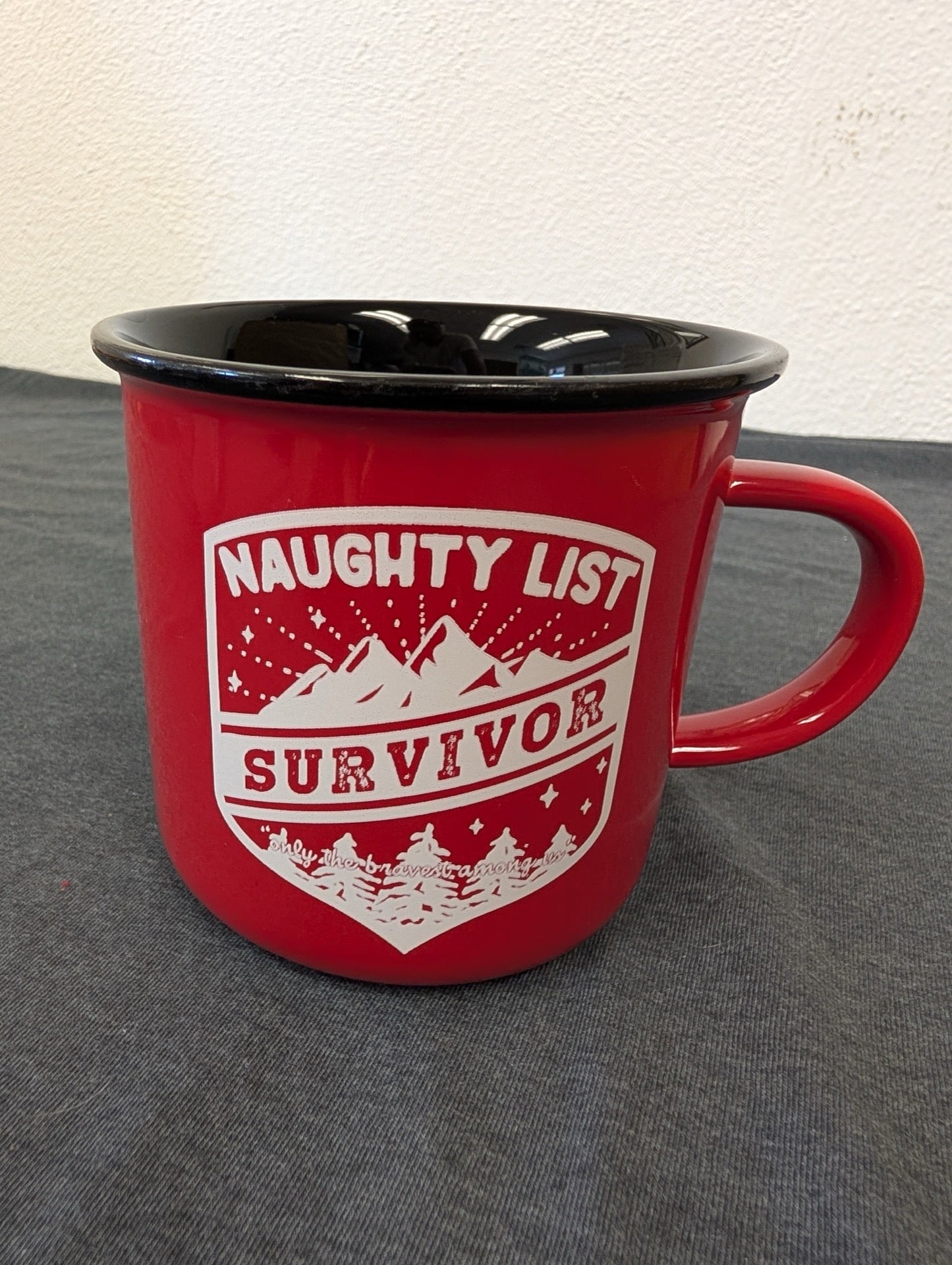 Red ceramic mug styled like an enamel camp cup with a white Naughty List Survivor mountain graphic.