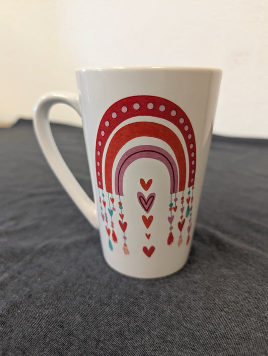 Tall white mug with a rainbow design made of red and pink hearts.