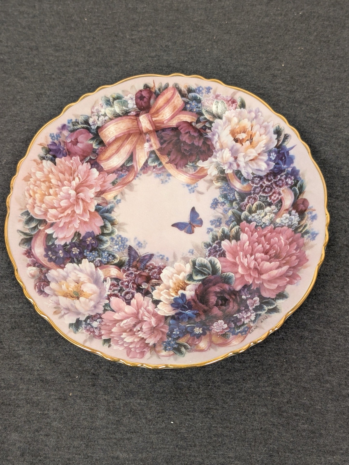 Porcelain plate featuring a dense wreath of pink peonies, purple flowers, and a blue butterfly.