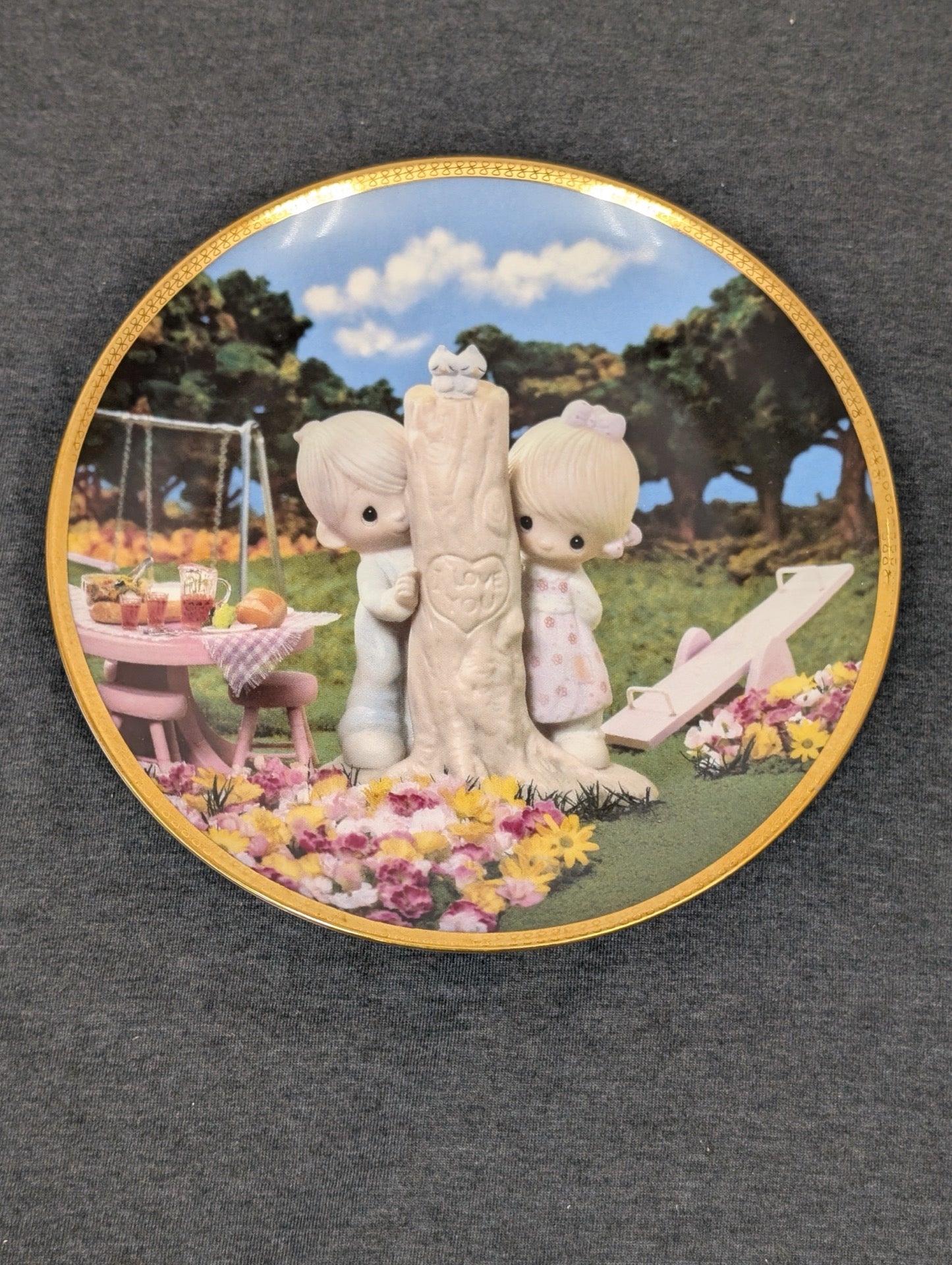 Collector plate showing a Precious Moments boy and girl peeking from behind a carved tree.
