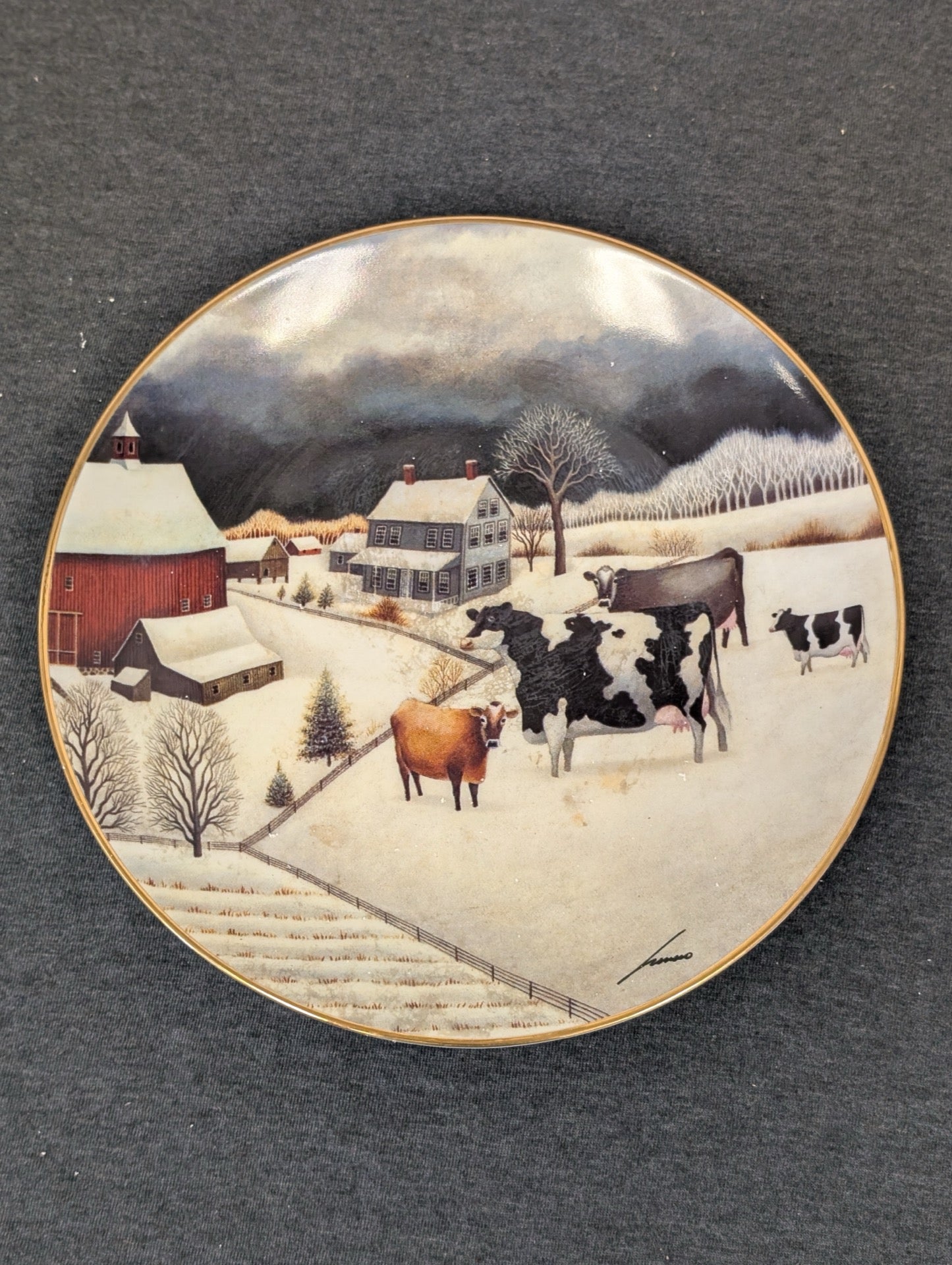 Porcelain plate showing stylized cows in a snowy farm landscape by Lowell Herrero.
