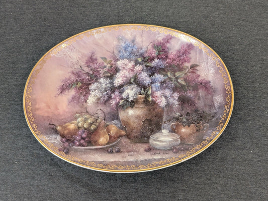 Oval porcelain plate featuring a still life painting of lilacs in a vase, pears, and grapes.