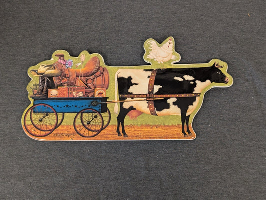 Shaped ceramic plaque of a black and white cow pulling a wagon, with a chicken on its back.