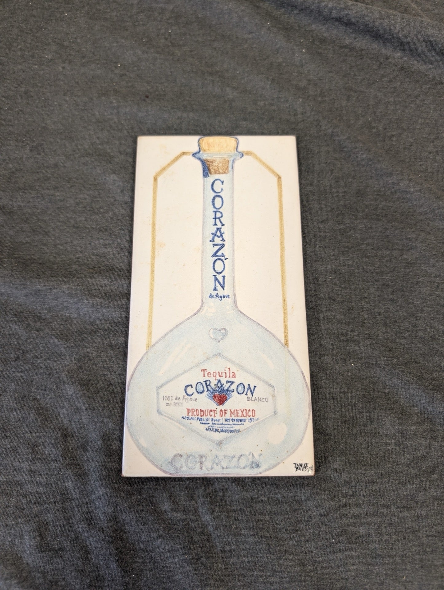 Rectangular ceramic tile featuring a drawing of a Tequila Corazon de Agave Blanco bottle.