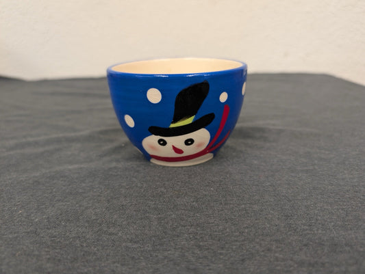 Small blue ceramic bowl with a hand-painted snowman face and white snowflakes on a gray background.
