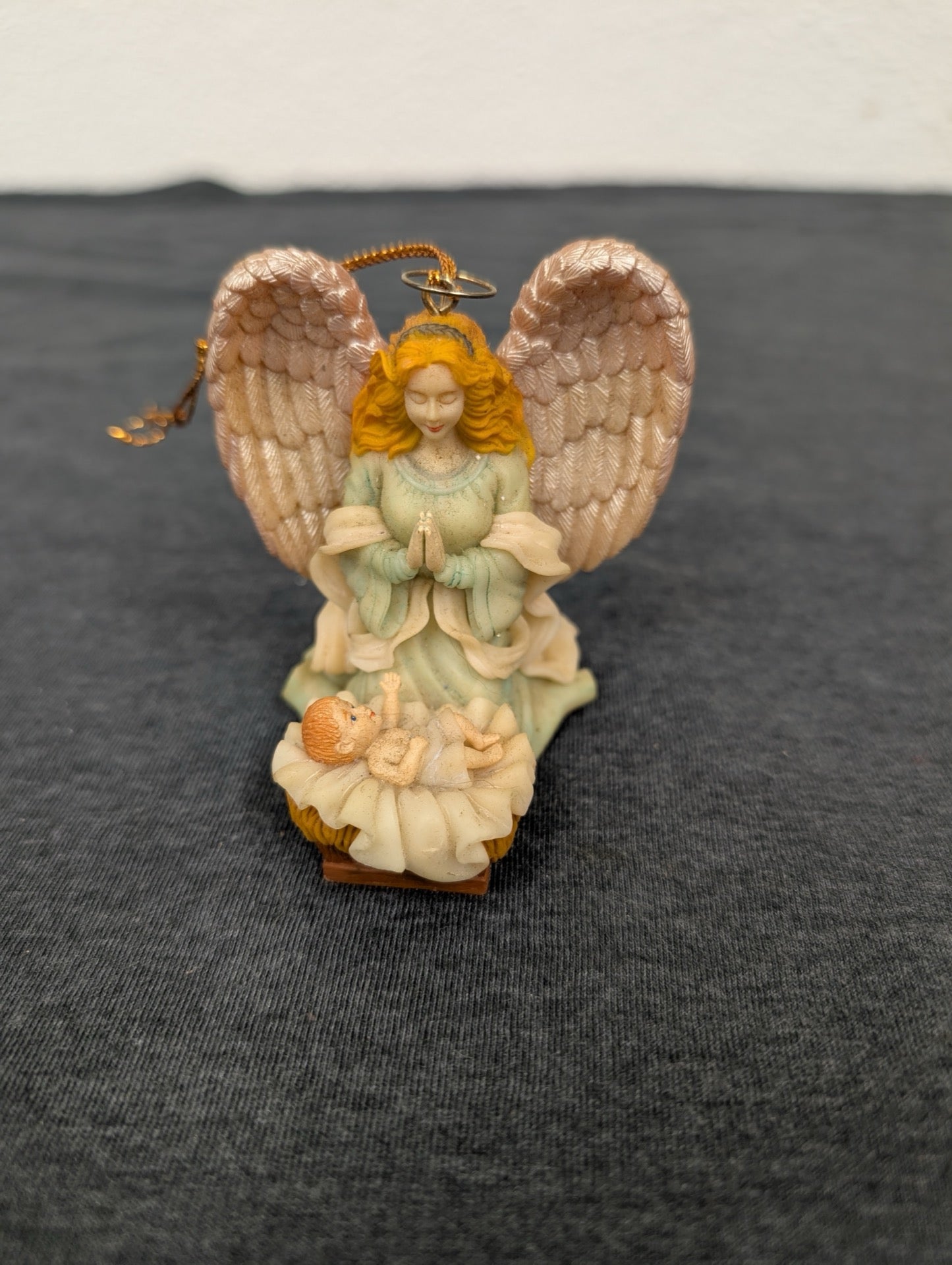 Small resin Christmas ornament of a blonde angel praying over a baby in a manger.