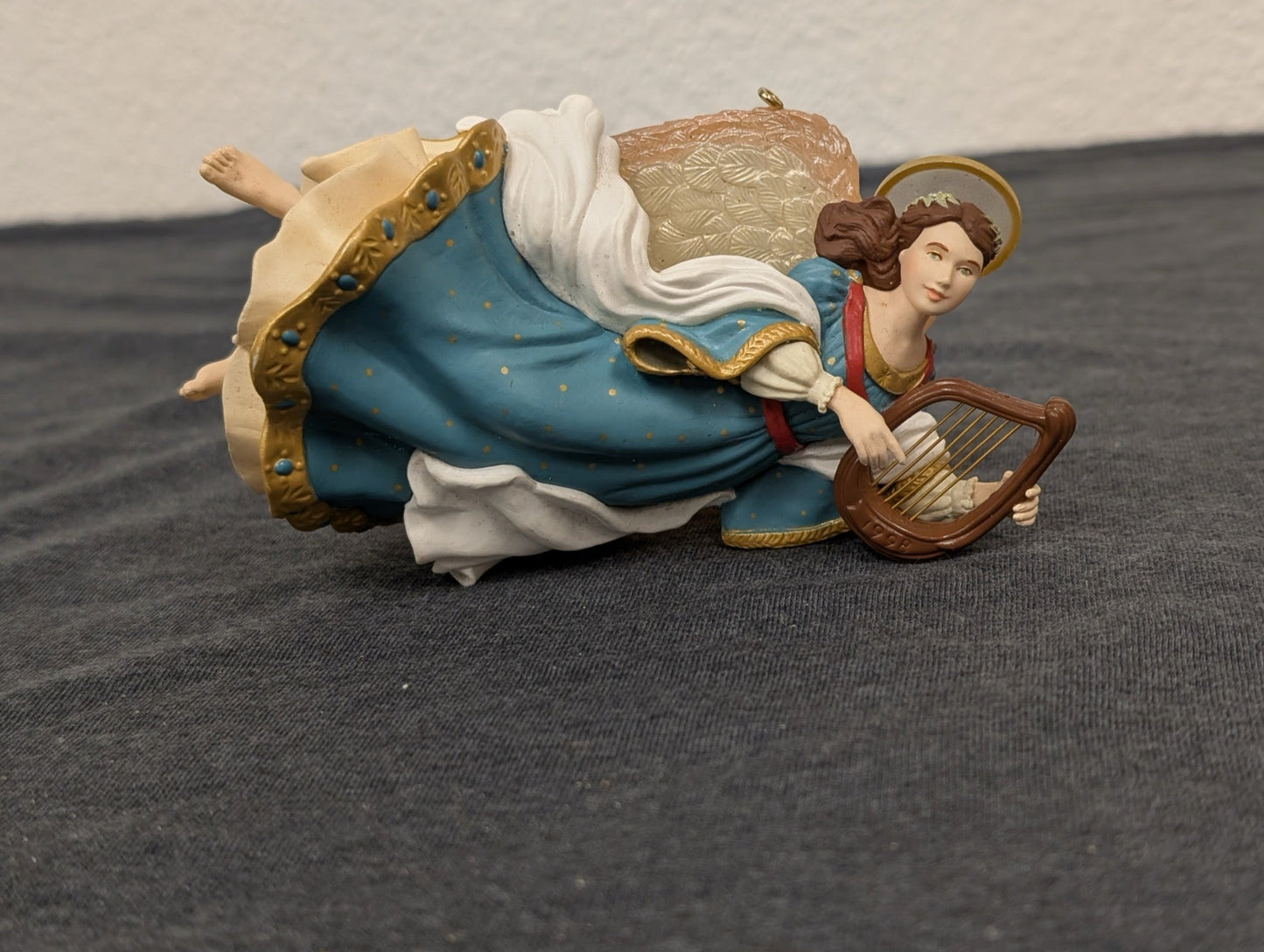 Resin Christmas ornament of a flying angel in a blue starry dress playing a brown harp.